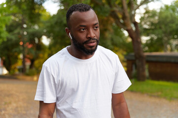 Serious young adult african american man walking in the park wearing headphones. Outdoor workouts