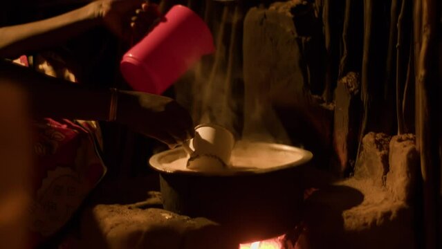Young african woman prepares food on fireplace in twig hut. Traditional dishes are prepared for whole family in large quantities