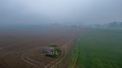 A foggy morning shows a wide rural landscape with fields and an old abandoned house, creating a calm atmosphere