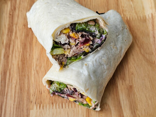 Tortilla wrap with tuna and vegetables on wooden plate. close up view