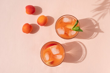 Top view of two glasses with refreshing iced peach fruit mocktail drinks and apricots on pastel...