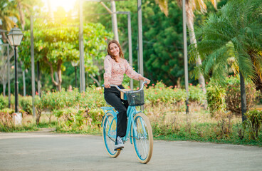 Obraz premium Portrait of smiling young woman riding a bicycle in a nice park. Happy girl riding a bicycle in a park at sunset