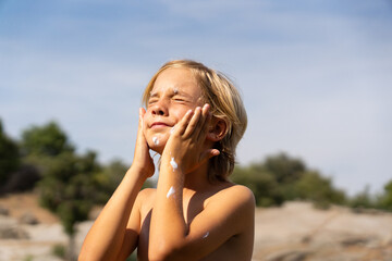Boy putting sunscreen on his face in nature