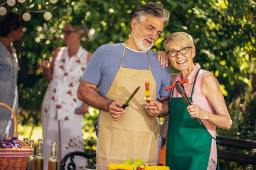 Elderly couple celebrate the 4th of July in their backyard. They are making barbeque, vegetables,...