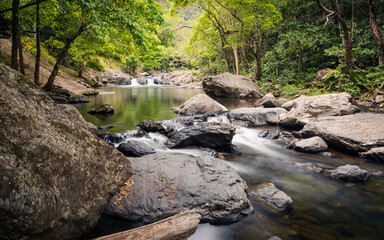 A tranquil creek with cascades and pools running between granite boulders and rainforest through a...