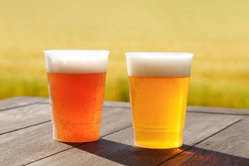 テーブルの上に２種類のビールが置かれている。プラスチックコップを使用。麦畑の背景