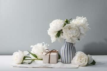 Fragrant white peonies in a vase and a gift box. Summer mood. Greeting card, copy space.
