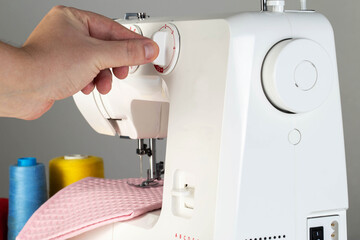The hand of a seamstress switches the stitch regulator on a sewing machine while sewing. Tailoring...