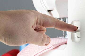 A seamstress's finger switches the reverse key of a sewing machine while sewing, close-up. Industry, regulator