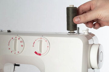Hand of a seamstress putting a spool of thread on a sewing machine while sewing, industry. Tailoring services, copy space for text