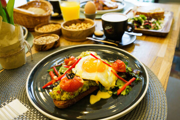Avocado toast with fried eggs and vegetables on a wooden table