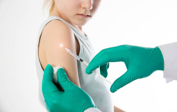 The hands of a doctor in green medical gloves make a vaccination against diphtheria, whooping cough and tetanus in the shoulder of a child girl. Copy space for text, revaccination