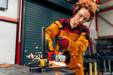Woman in STEM using grinder to cut a metal bar, wearing gloves and a apron with protective sleeves. She's making a new metal part for her engineering project © DusanJelicic