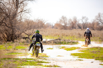 Fototapeta premium A motorcyclist rides an enduro motorcycle off-road. Driving through swampy areas, water and mud splashing from under the wheels. Kazakhstan, Shymkent - April 17, 2024