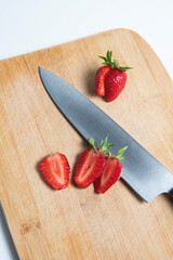 The strawberries are cut into slices. they lie on a wooden board and next to the knife