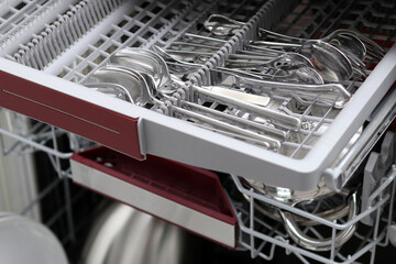 Close up of cutlery in a dishwasher, grey rack