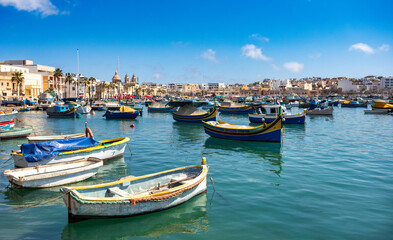 Fototapeta premium Traditional eyed colorful boats Maltese Luzzu in the turquoise blue water in the Harbor of Mediterranean fishing village Marsaxlokk, Cultural heritage of Malta.