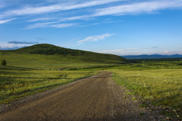 A dirt road leading to green hills against a blue sky