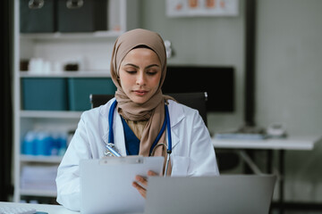Female in uniform of doctor using digital technology laptop for Output Device and writing a patient report on the office desk.
