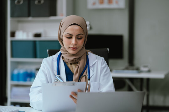Female in uniform of doctor using digital technology laptop for Output Device and writing a patient report on the office desk.