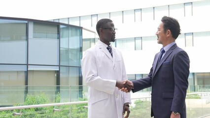 A black man in a white coat and a businessman shaking hands