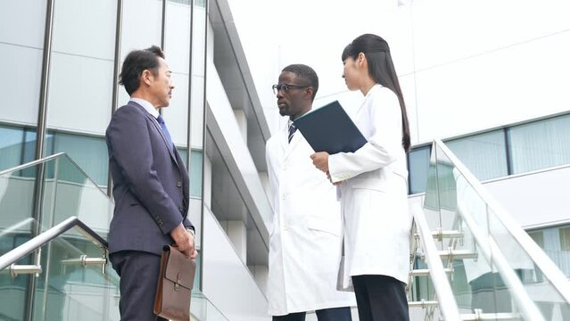 ロビーで会話するビジネスマンと白衣の多国籍技術者グループ
