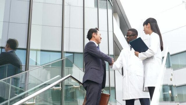 Businessman and a group of multinational engineers in white coats shaking hands in a lobby