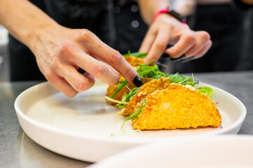Close-up of hand garnishing taco appetizers on a plate, highlighting fresh ingredients and culinary presentation