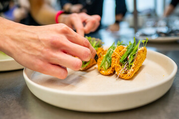 Close-up of hand garnishing taco appetizers on a plate, highlighting fresh ingredients and culinary presentation