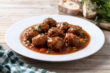 Meatballs, green peas and carrot with tomato sauce on wooden table