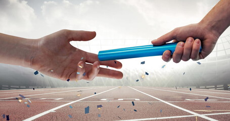 Confetti falling over close up of a hand passing a baton against sports field