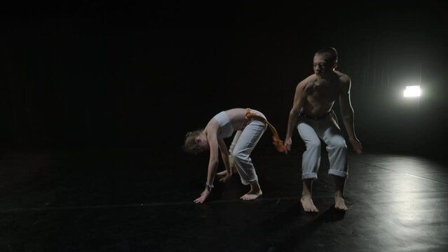 Capoeira fighters performing dynamic moves on stage. Martial arts, dance, and acrobatics in action. Bare-chested athletes showcasing strength, flexibility, and technique under spotlights