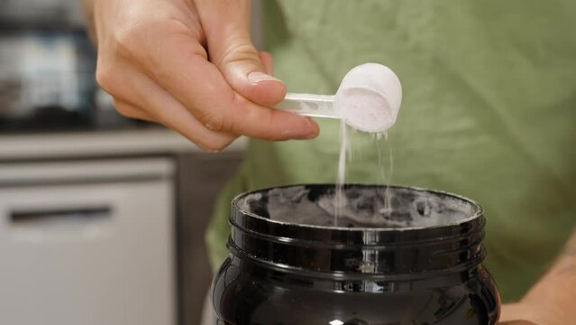 Man Showing White Powder in a Black Jar with a Measuring Spoon Inside. Sports Supplement Creatine.