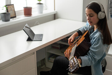 Teenager girl learning to play guitar at home using online lessons. Hobby remote musical education...