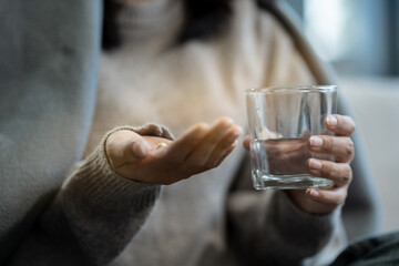 Depressed woman holding a glass of water, suffering from headaches, fighting stress with antidepressants, close-up view.