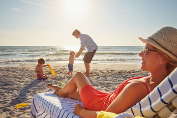 Chair, relax or children with woman at beach on holiday vacation or weekend together with dad or family. Father, calm mother or kids siblings at sea for bonding or break in nature in Spain in summer