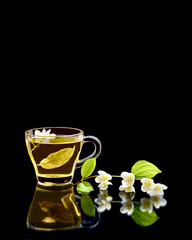 Green tea with jasmine and a cup with hot fresh tea on a black background on a reflective surface