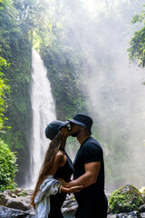 Romantic moment as a couple kisses amidst the misty backdrop of a lush waterfall, symbolizing love and connection.