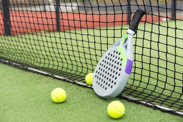 Closeup view of a paddle racket and balls in a padel tennis court near the net. Green background...