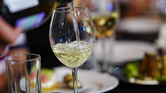 White wine is poured into a glass on the banquet table. alcoholic and soft drinks for the celebration. work as a sommelier or waiter.
