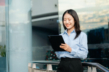 Asian woman with a smile standing holding notepad and tablet at out side office. big city on...