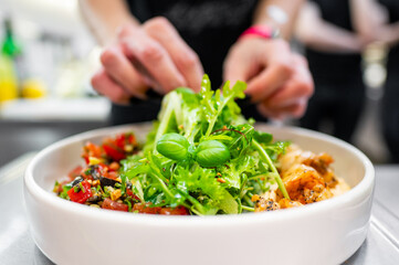 Close-up of a hand garnishing a dish with herbs, featuring grilled shrimp and fresh salad.