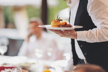waiter in a stylish uniform carrying an exquisite dish to a client in a beautiful gourmet restaurant. Table service in the restaurant.