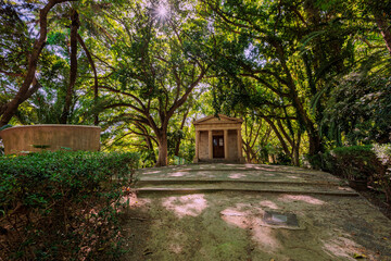 Sun shining through trees on small stone doric temple building in park