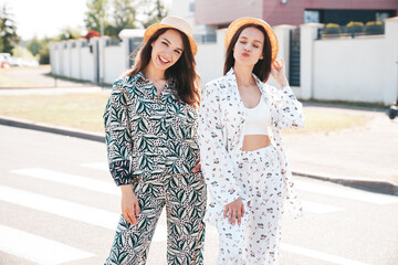 Two young beautiful smiling hipster female in trendy summer costumes  clothes. Sexy carefree women posing in the street. Positive models having fun at sunny day. Going crazy. In hat