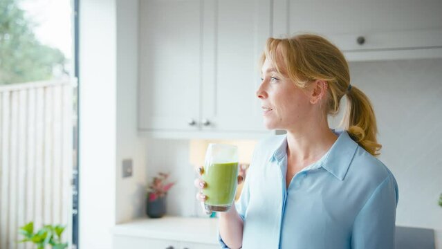 Woman drinking fresh healthy green smoothie made from apples,banana and celery from glass in kitchen at home - shot in slow motion