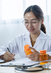Female doctor holding a medicine bottle is checking the quality of medicine for any side effects the patient or not and recording patient information at the hospital. medical and health care concept