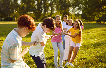 Group of a happy joyful smiling children playing together in tug-of-war with a rope in the park on...