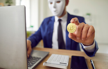 Anonymous man wearing mask, working on laptop and holding a bitcoin coin. Digital realm of finance,...