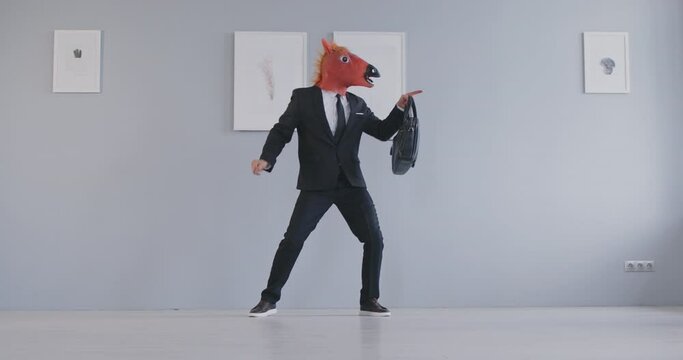 Excited funny business man wearing suit and horse animal mask holding bag having fun and dancing in office indoors rejoicing making of successful deal. Entertainment and fun concept. 4k video.